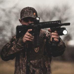 Tactical shooter holding rifle equipped with matte black vertical grip laser flashlight combo featuring 500-lumen light