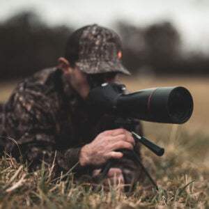 Man using Osprey Spotting Scope 20-60x80 outdoors on grass with camouflage clothing and cap